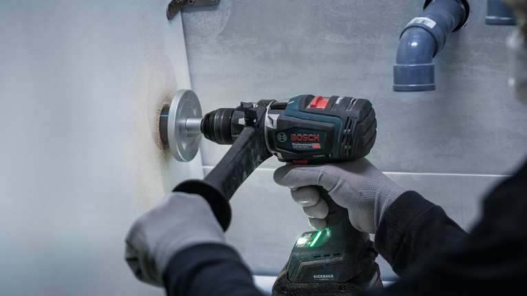 안전 장비를 착용한 사람이 전동 공구로 벽에 구멍을 뚫고 있다.