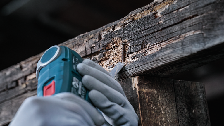 안전 장비를 착용한 사람이 전동 공구를 사용하여 손상된 나무에서 못을 뽑아내고 있습니다.