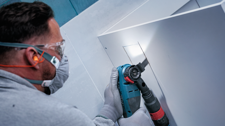 안전 장비를 착용한 사람이 전동 공구를 이용해 패널을 절단하고 있습니다.