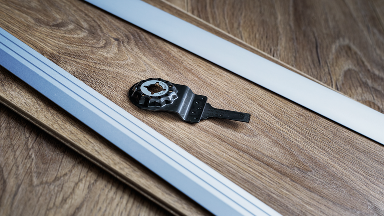 진동 공구 날과 가이드 레일이 나무 바닥 표면에 놓여 있습니다.