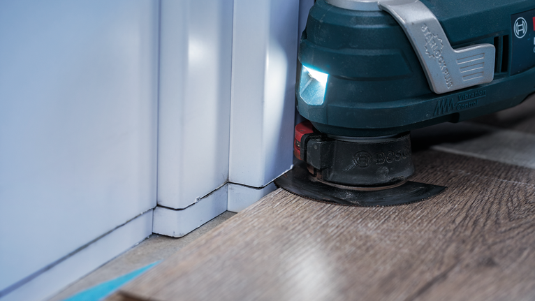 벽 근처에서 라미네이트 바닥재를 다듬는 진동식 다용도 공구.