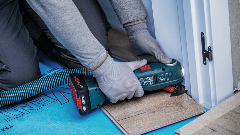 안전 장비를 착용한 사람이 무선 공구를 사용하여 라미네이트 바닥재를 자르고 있습니다.