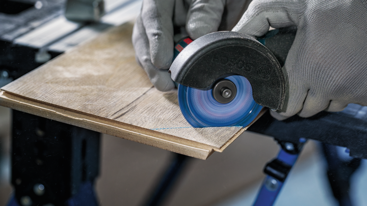 안전 장비를 착용한 사람이 각도 그라인더로 나무판을 자르고 있습니다.