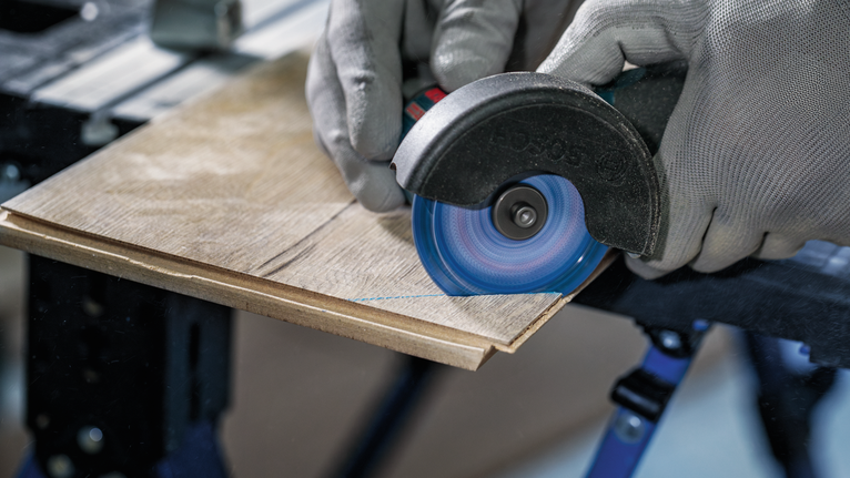 안전 장비를 착용한 사람이 각도 그라인더로 나무판을 자르고 있습니다.