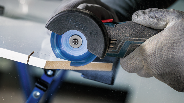 안전 장비를 착용한 사람이 원형 톱을 사용하여 시트 소재를 자릅니다.