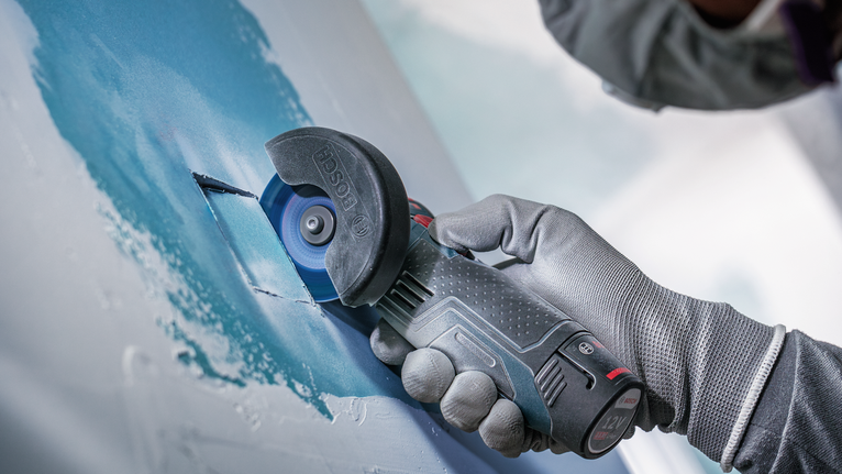 안전 장비를 착용한 사람이 전동 절단기를 사용하여 건식벽체를 자르고 있습니다.