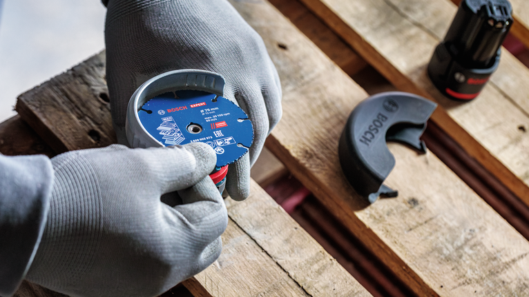 안전 장비를 착용한 사람이 나무 팔레트에 분쇄 디스크를 부착하고 있습니다.