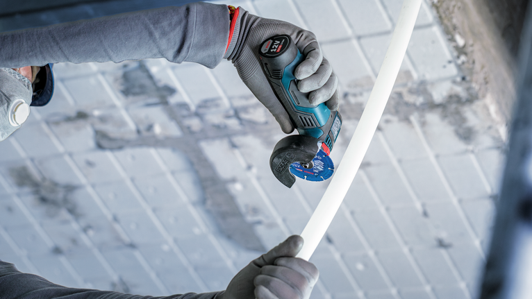 안전 장비를 착용한 사람이 회전 도구로 흰색 파이프를 자릅니다.