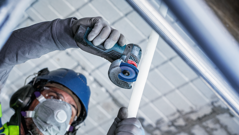 안전 장비를 착용한 사람이 소형 전동 공구로 흰색 파이프를 자르고 있습니다.