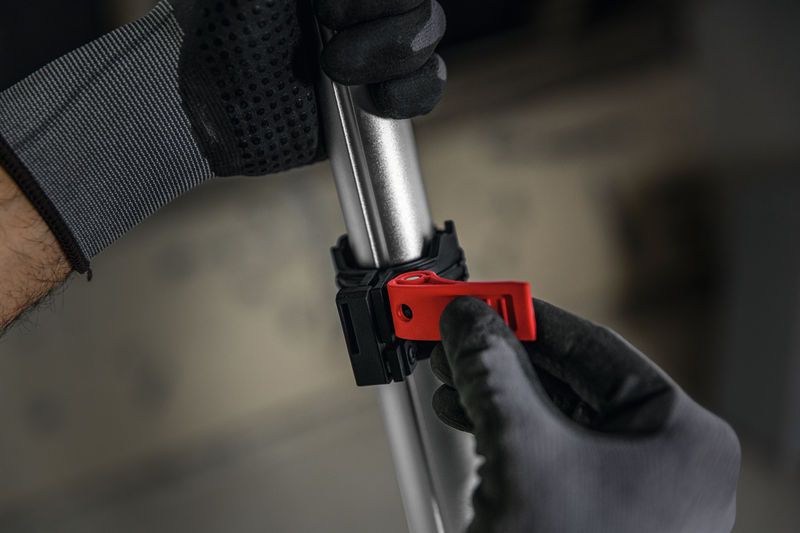 안전 장비를 착용한 사람이 금속 막대에 있는 빨간색 클램프를 조정하고 있습니다.