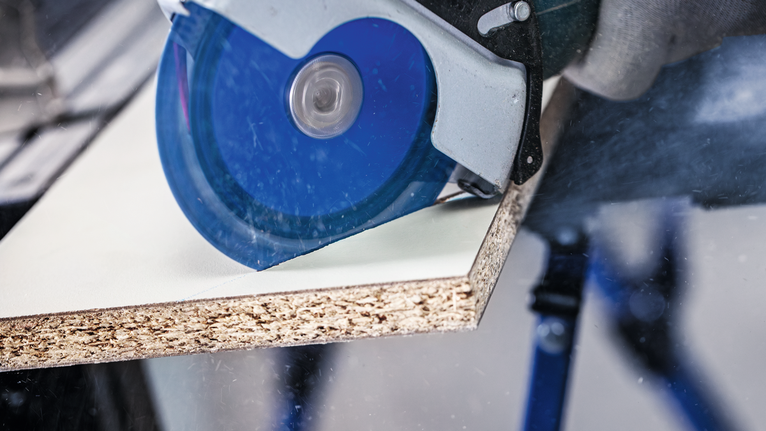 안전 장비를 착용한 사람이 원형 톱으로 나무판을 자르고 있습니다.