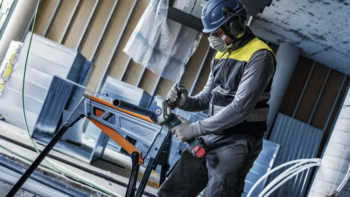 안전 장비를 착용한 사람이 작업대 위의 금속 튜브에 구멍을 뚫고 있습니다.