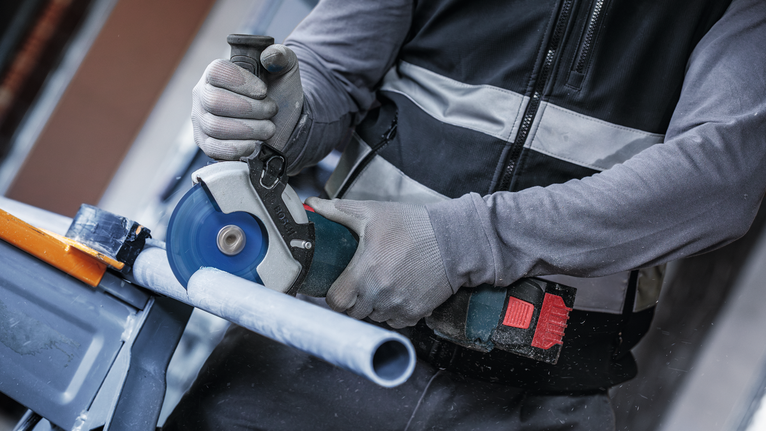 안전 장비를 착용한 사람이 원형 톱으로 플라스틱 파이프를 자릅니다.