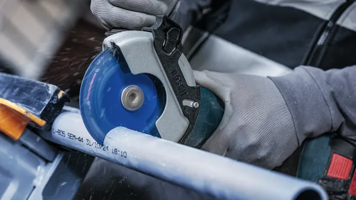 안전 장비를 착용한 사람이 원형 톱으로 플라스틱 파이프를 자릅니다.