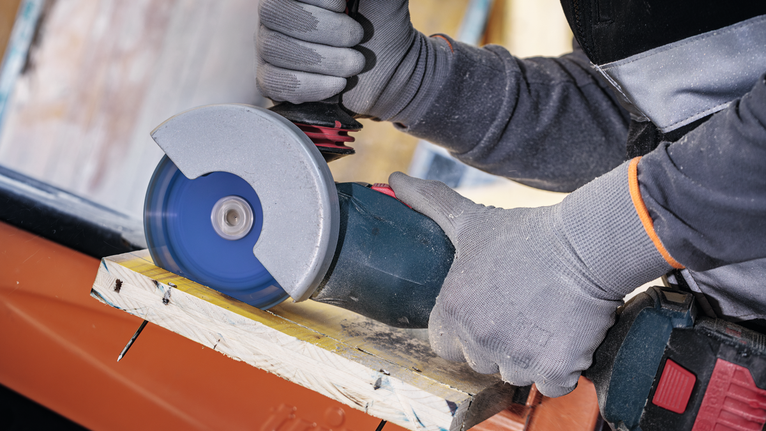 안전 장비를 착용한 사람이 각도 그라인더로 나무를 자릅니다.