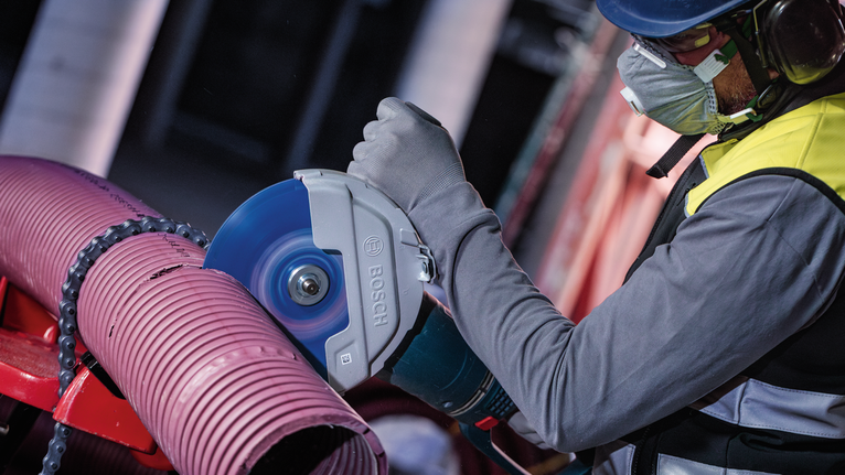 안전장비를 착용한 사람이 전동 절단기로 큰 플라스틱 파이프를 자릅니다.