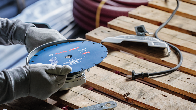 안전 장비를 착용한 사람이 나무 팔레트 위에서 전동 공구를 조정하고 있습니다.