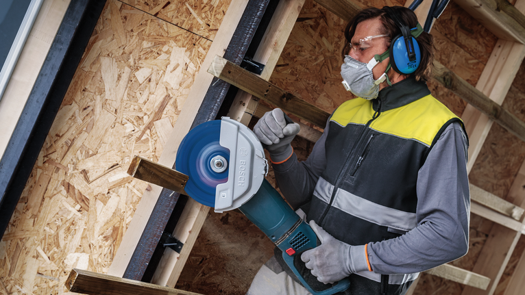 안전 장비를 착용한 사람이 큰 원형 톱으로 나무를 자릅니다.