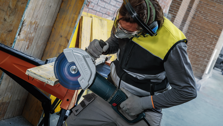 안전 장비를 착용한 사람이 큰 원형 톱으로 나무 판자를 자릅니다.