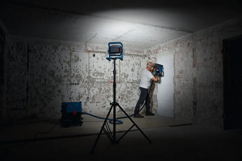 안전 장비를 착용한 사람이 작업등 아래에서 벽 드릴링 도구를 조작하고 있습니다.