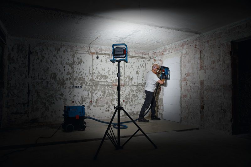 안전 장비를 착용한 사람이 작업등 아래에서 벽 드릴링 도구를 조작하고 있습니다.