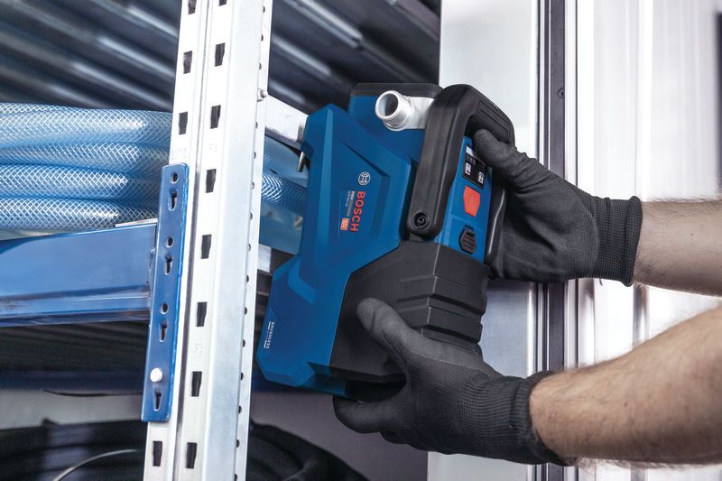 안전 장비를 착용한 사람이 금속 선반 근처에 파란색 전동 공구를 설치하고 있습니다.