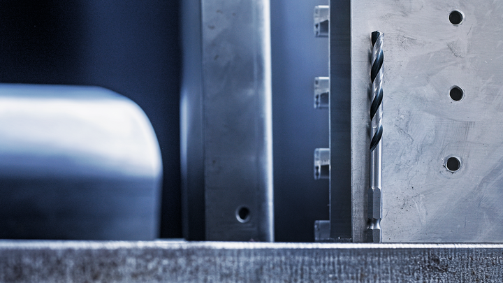 기계로 가공된 금속 표면에 수직으로 배치된 금속 드릴 비트입니다.