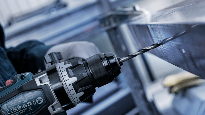 안전장비를 착용한 사람이 금속 빔에 구멍을 뚫고 있습니다.