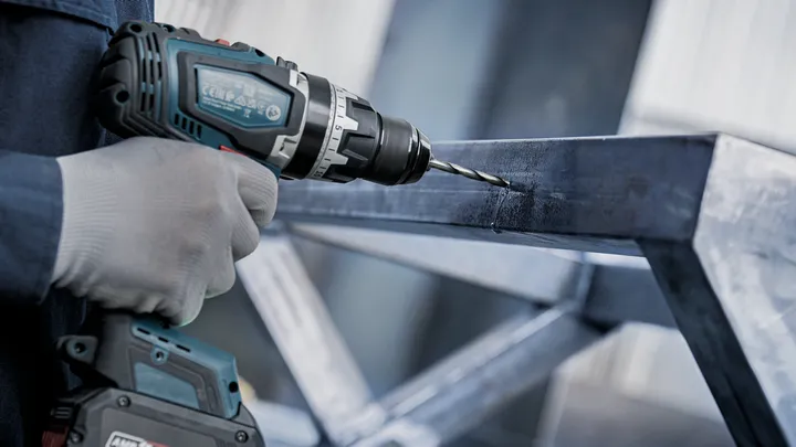 안전 장비를 착용한 사람이 금속 빔에 구멍을 뚫고 있습니다.