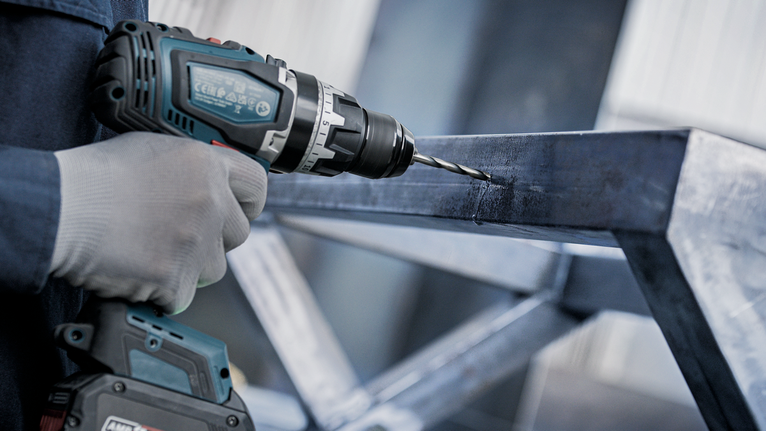 안전 장비를 착용한 사람이 금속 빔에 구멍을 뚫고 있습니다.