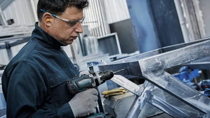 안전장비를 착용한 사람이 금속 프레임에 구멍을 뚫고 있습니다.