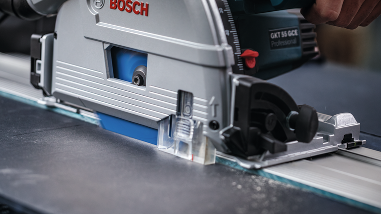 안전 장비를 착용한 사람이 직선 금속 레일을 따라 원형 톱을 안내합니다.