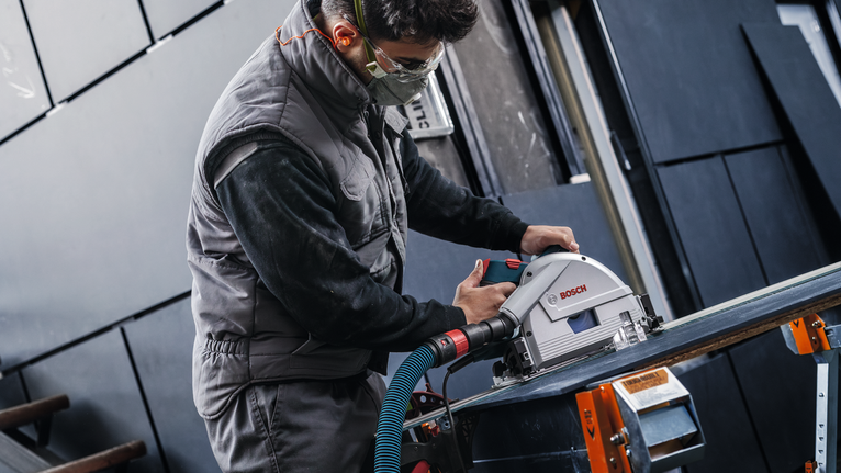 안전 장비를 착용한 사람이 작업대 위에서 전동 공구를 이용해 돌을 자르고 있습니다.