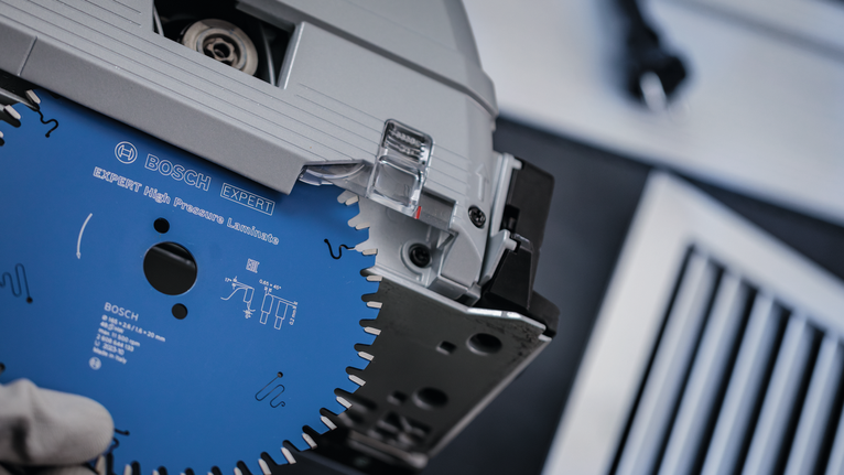 안전 장비를 착용한 사람이 전동 공구에 원형 톱날을 설치하고 있습니다.