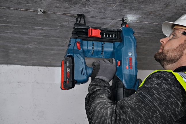 안전장비를 착용한 사람이 천장에 구멍을 뚫어 금속 옷걸이를 설치하고 있습니다.