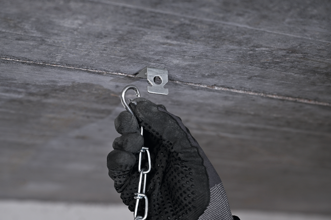 안전 장비를 착용한 사람이 금속 천장 걸이에 사슬을 걸고 있습니다.