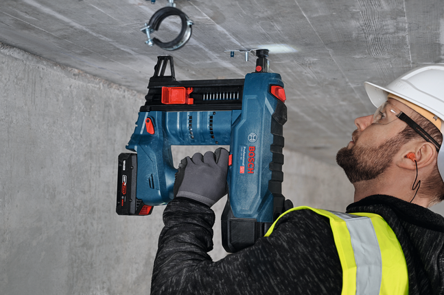 안전 장비를 착용한 사람이 전동 공구를 사용하여 외부 나사산 M8이 있는 금속 옷걸이를 설치합니다.