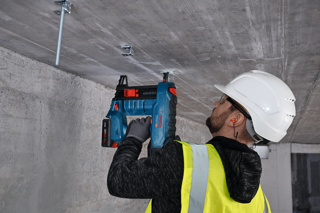 안전 장비를 착용한 사람이 콘크리트 천장에 금속 옷걸이를 고정하고 있습니다.