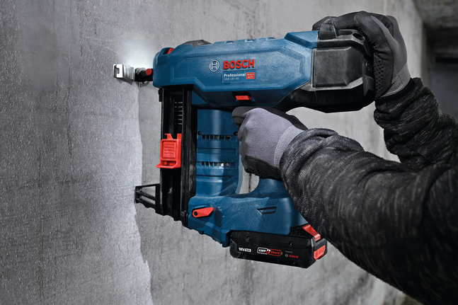 안전 장비를 착용한 사람이 콘크리트 벽에 금속 케이블 타이 마운트를 고정하고 있습니다.