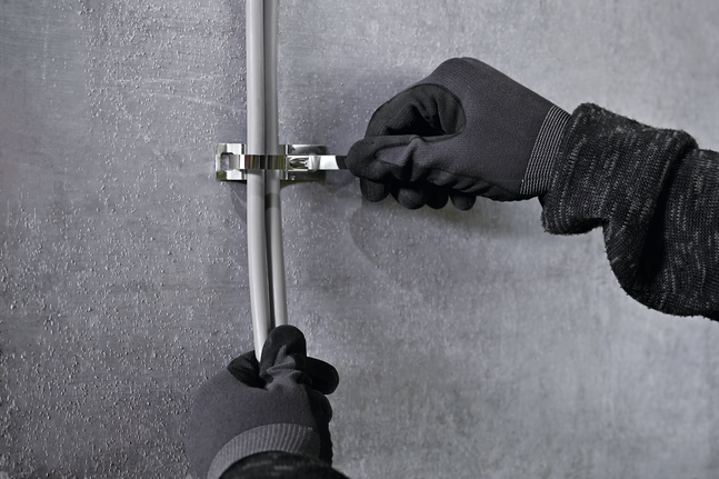 안전 장비를 착용한 사람이 금속 케이블 타이 마운트를 이용해 케이블을 벽에 고정하고 있습니다.