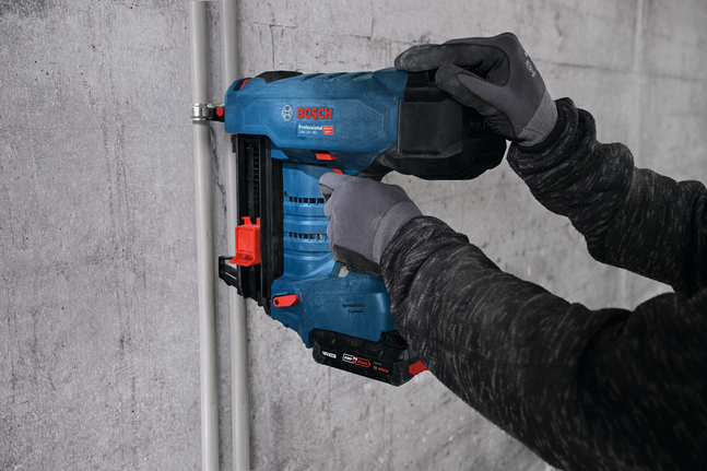 안전 장비를 착용한 사람이 무선 못 박는 기계를 사용하여 콘크리트 벽에 전선관을 고정하고 있습니다.