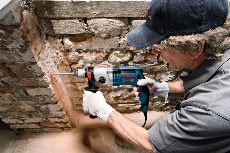 안전장비를 착용한 사람이 돌담에 구멍을 뚫고 있습니다.