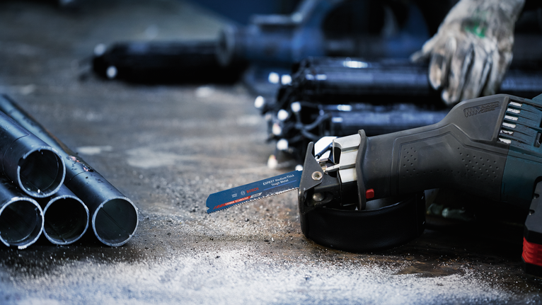 안전 장비를 착용한 사람이 금속 파이프 근처에서 왕복톱을 사용하고 있습니다.