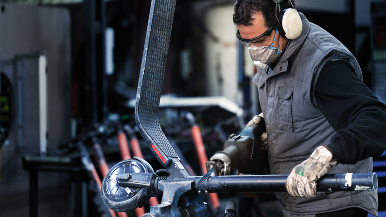 안전 장비를 착용한 사람이 전동 공구를 사용하여 금속 튜브를 절단하고 있습니다.