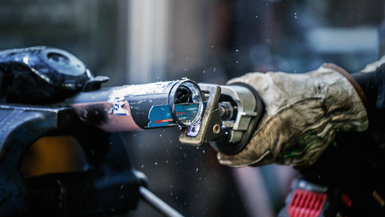 안전 장비를 착용한 사람이 전동 공구로 금속 파이프를 자르고 있습니다.