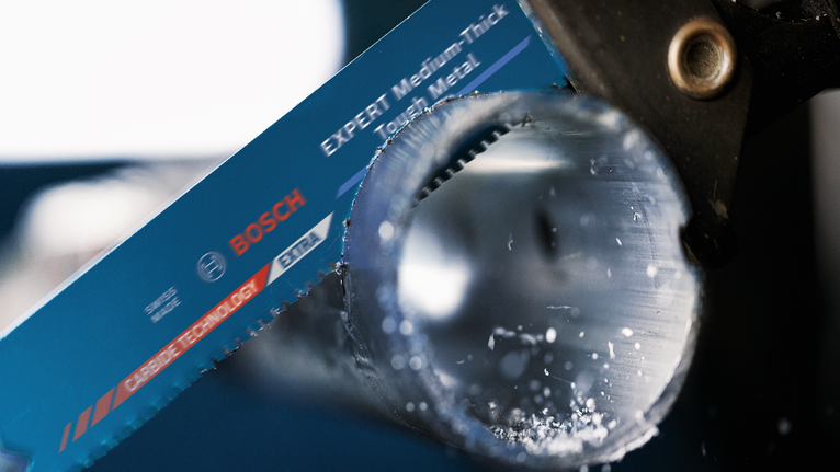 톱날이 금속 파이프를 절단하는 모습이며, 금속 부스러기가 보인다.