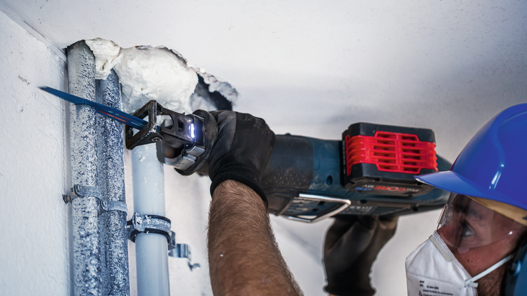 안전 장비를 착용한 사람이 왕복톱을 사용하여 파이프를 절단하고 있습니다.