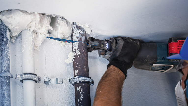 안전 장비를 착용한 사람이 전동 공구를 사용하여 금속 파이프를 절단하고 있습니다.