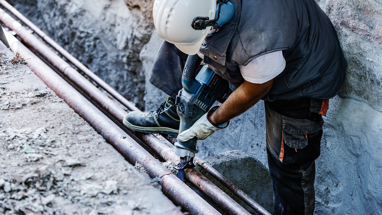 안전 장비를 착용한 사람이 전동 공구를 사용하여 야외에서 금속 파이프를 절단하고 있습니다.