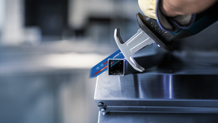 안전 장비를 착용한 사람이 왕복톱으로 금속 사각관을 자르고 있습니다.